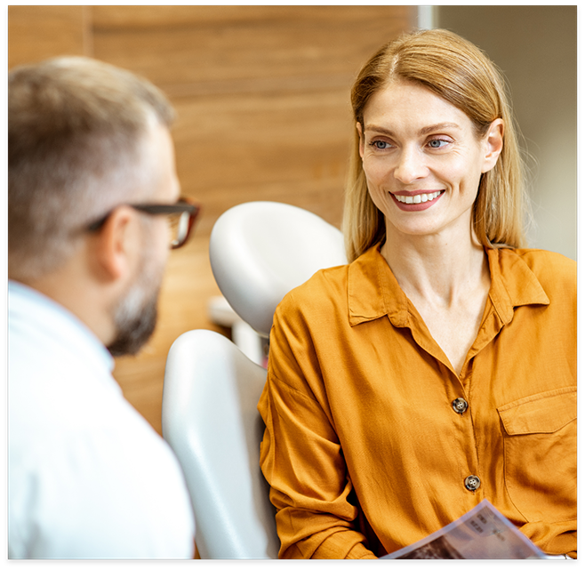 Woman in orange shirt sitting in dental chair and talking to dentist in Cottonwood Heights