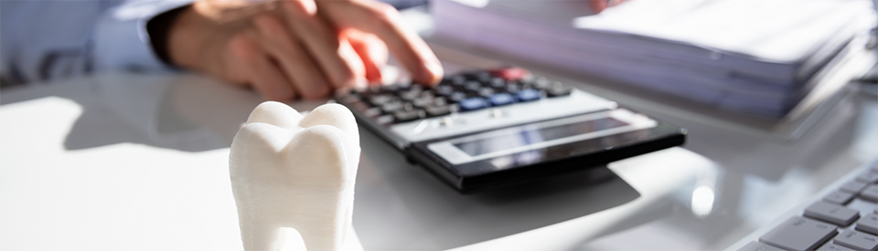 Person using calculator with model of tooth nearby