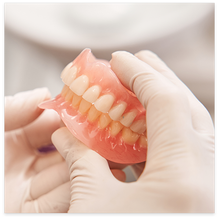 Gloved hands holding full dentures