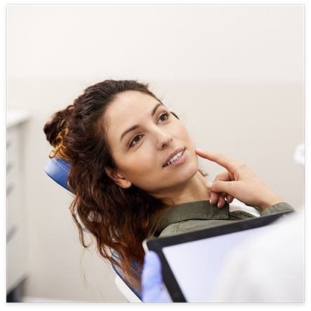 Woman in dental chair pointing to her jaw