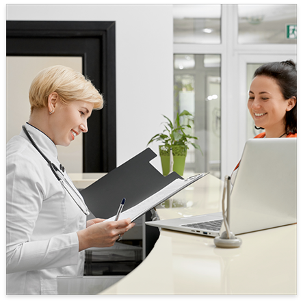 Dentist at front desk looking at folder while speaking to patient