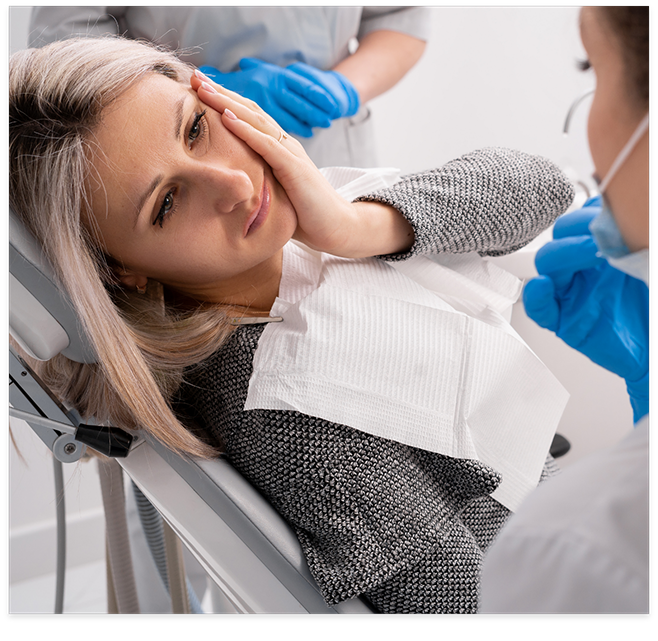 Woman in dental chair rubbing jaw in pain