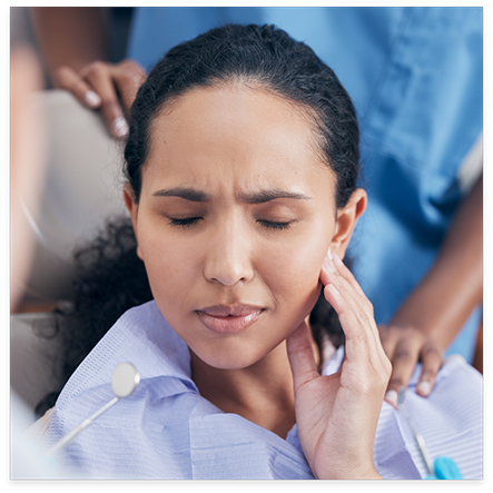 Woman rubbing jaw with dentists standing around her