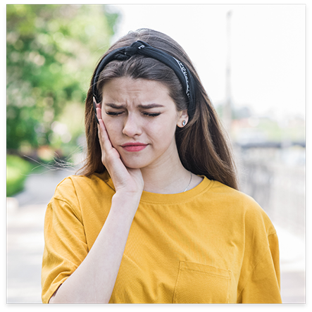 Woman in yellow shirt rubbing jaw in pain