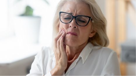 Senior woman with glasses rubbing jaw in pain