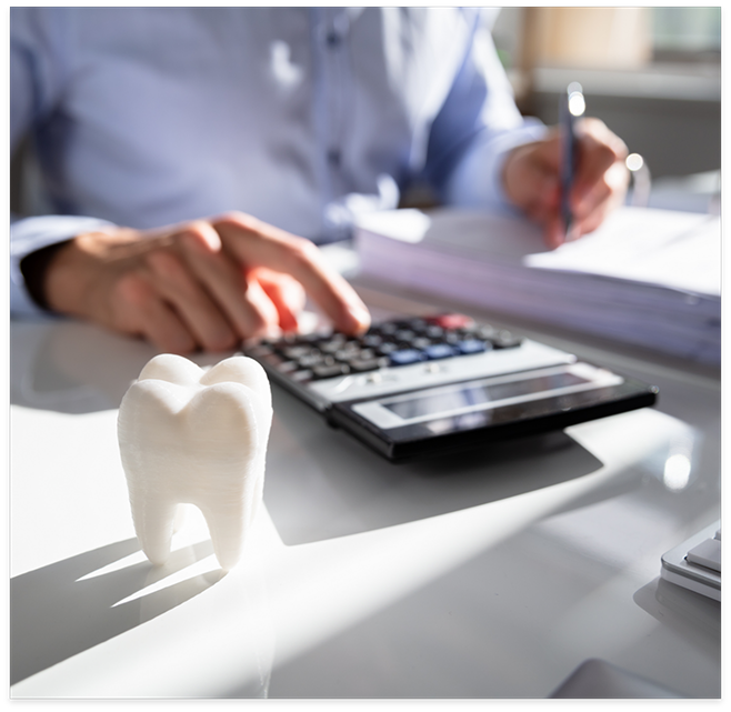 Person using calculator on desk with tooth sitting on it