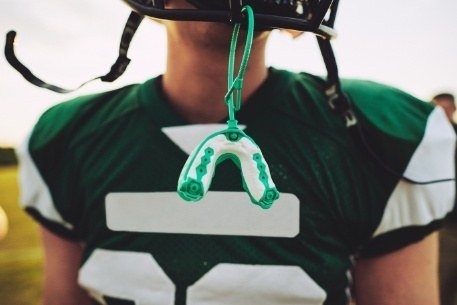 Teen with green mouthguard hanging from football helmet