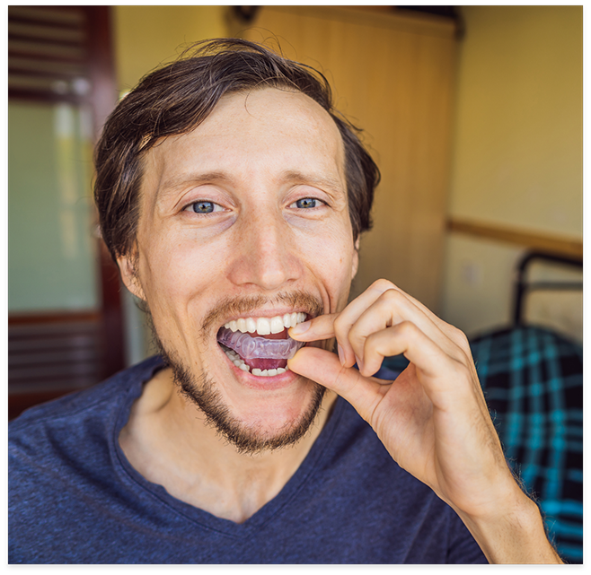 Man putting in a nightguard while standing in front of bed