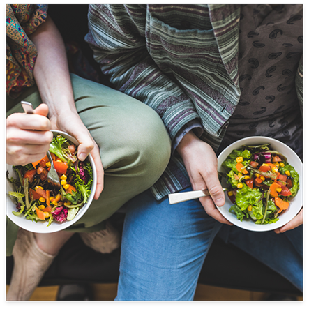 Close up of two people holding salads