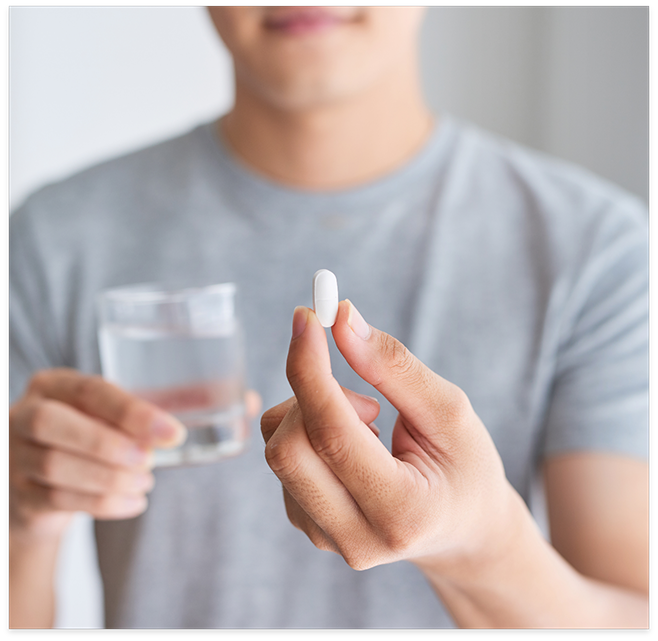 Man in grey shirt holding pill and glass of water