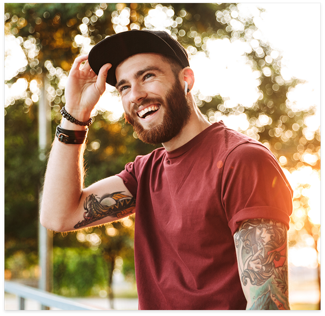 Young man with beard and baseball cap smiling outside