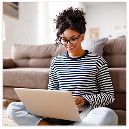 Smiling woman sitting in front of couch and using a laptop