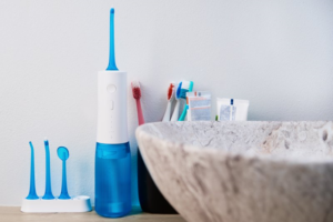 Water flosser, toothbrushes, and toothpaste sitting behind bathroom sink