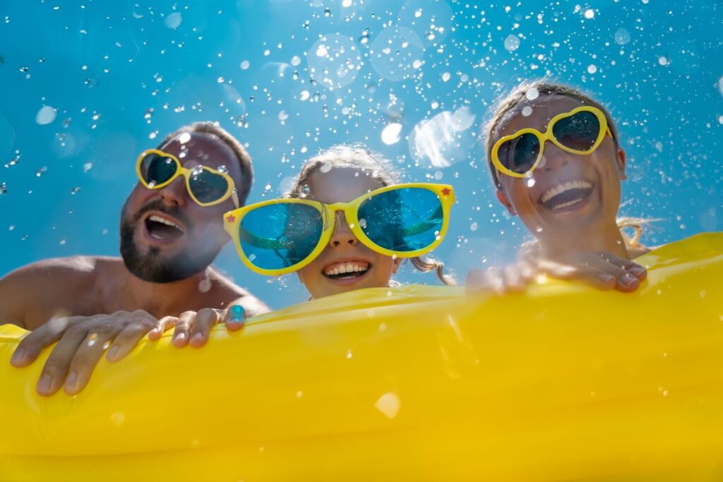 A man, woman, and child in sunglasses smiling on a pool float.