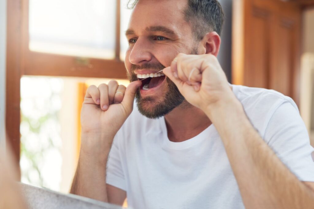 A man flossing his teeth in front of a mirror